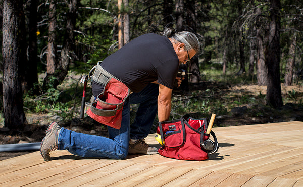 A person repairing a wooden the deck with The Truck filled with tools.